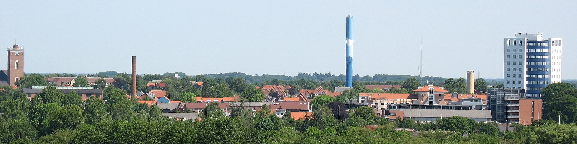 Panorama af Herning set fra oven med røde tage, træer, kirke og blåt vandtårn i klart dagslys